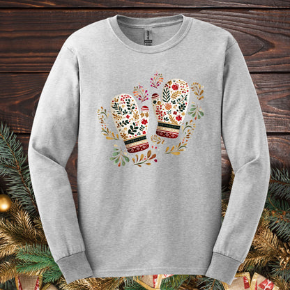 Ash long sleeve tee with watercolor folk art mittens in red, cream, evergreen, and gold, surrounded by winter foliage.