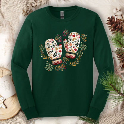 Forest Green long sleeve tee with folk art watercolor mittens in red, cream, evergreen, and gold, surrounded by winter foliage.