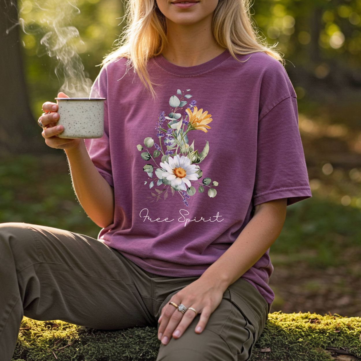 Woman in a plum garment-dyed "Free Spirit" t-shirt with a hand-painted botanical bouquet, holding a mug.