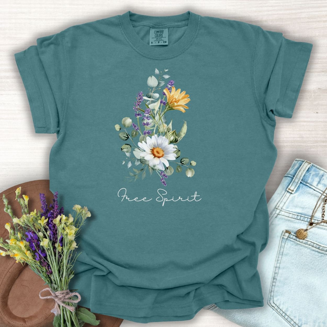 Blue Spruce S t-shirt with a hand-painted daisy, lavender, eucalyptus bouquet, and "Free Spirit" script.