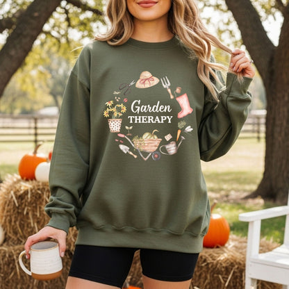 Woman in a green "Garden Therapy" sweatshirt with a floral wreath of gardening tools, holding a mug.