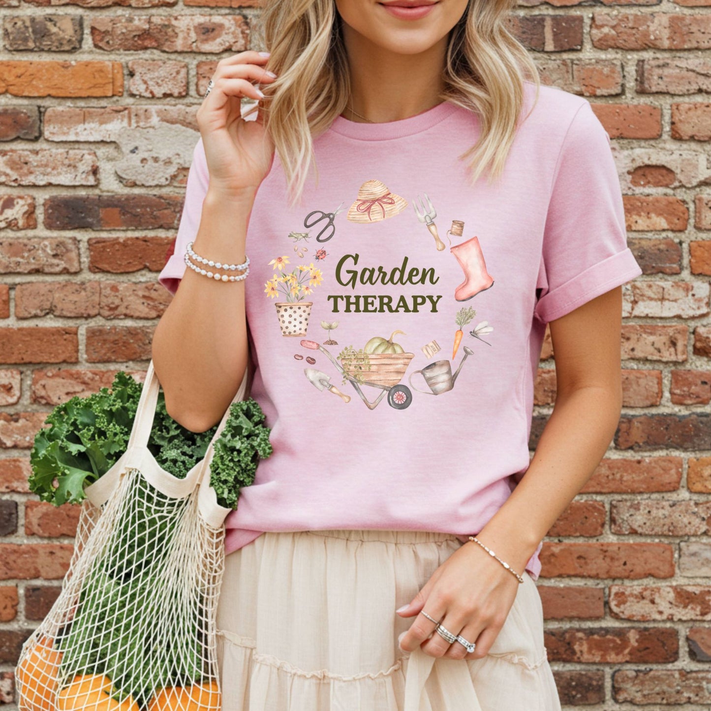 Woman in a pink Garden Therapy t-shirt with a floral wreath design, holding a mesh bag of produce.
