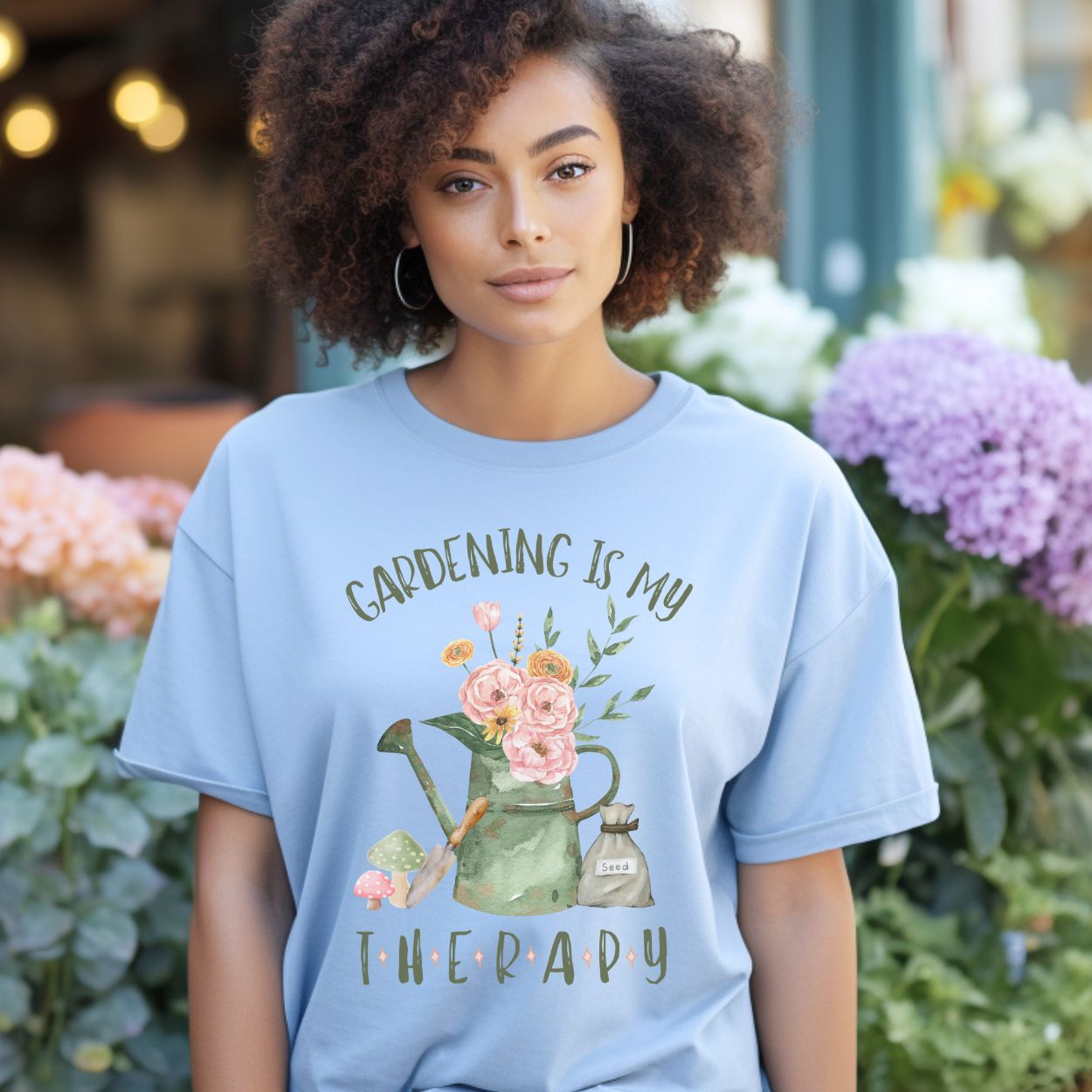 Woman wearing a light blue cotton t-shirt with a "Gardening Is My Therapy" floral watering can design.