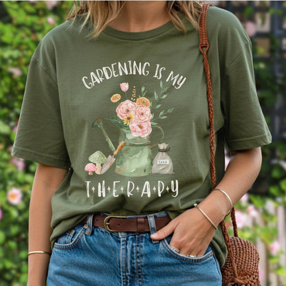 Olive green cotton t-shirt with "Gardening Is My Therapy" and a watercolor watering can, flowers, trowel, mushrooms, and seed bag.