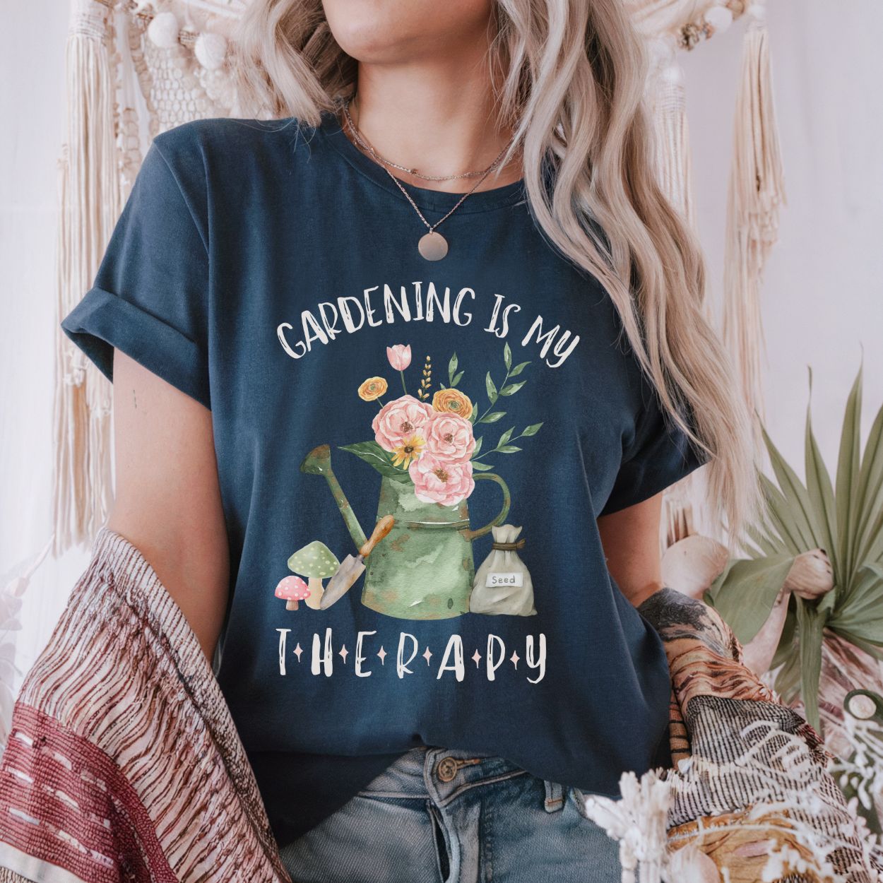 Woman in a navy blue "Gardening Is My Therapy" t-shirt with a watercolor watering can, flowers, and seed bag design.