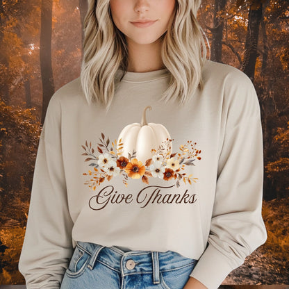 Woman wearing a beige long sleeve tee with a watercolor white pumpkin, autumn foliage, and "Give Thanks" text.
