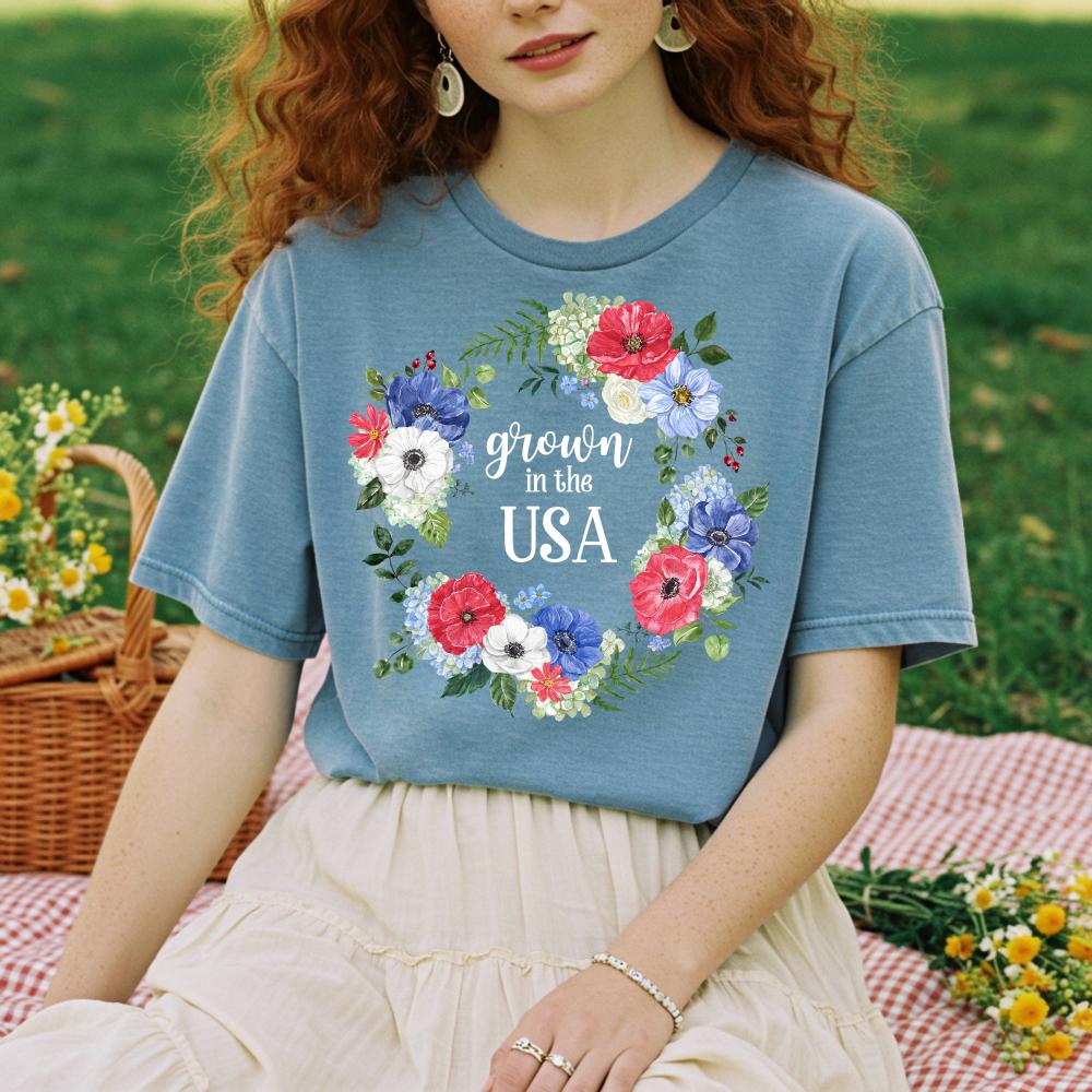 young woman wearing a blue t-shirt with floral design and 'grown in the USA' text, sitting outdoors.