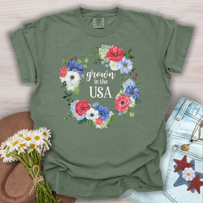 Moss green t-shirt with "Grown in the USA" in a floral wreath of red, white, and blue flowers.