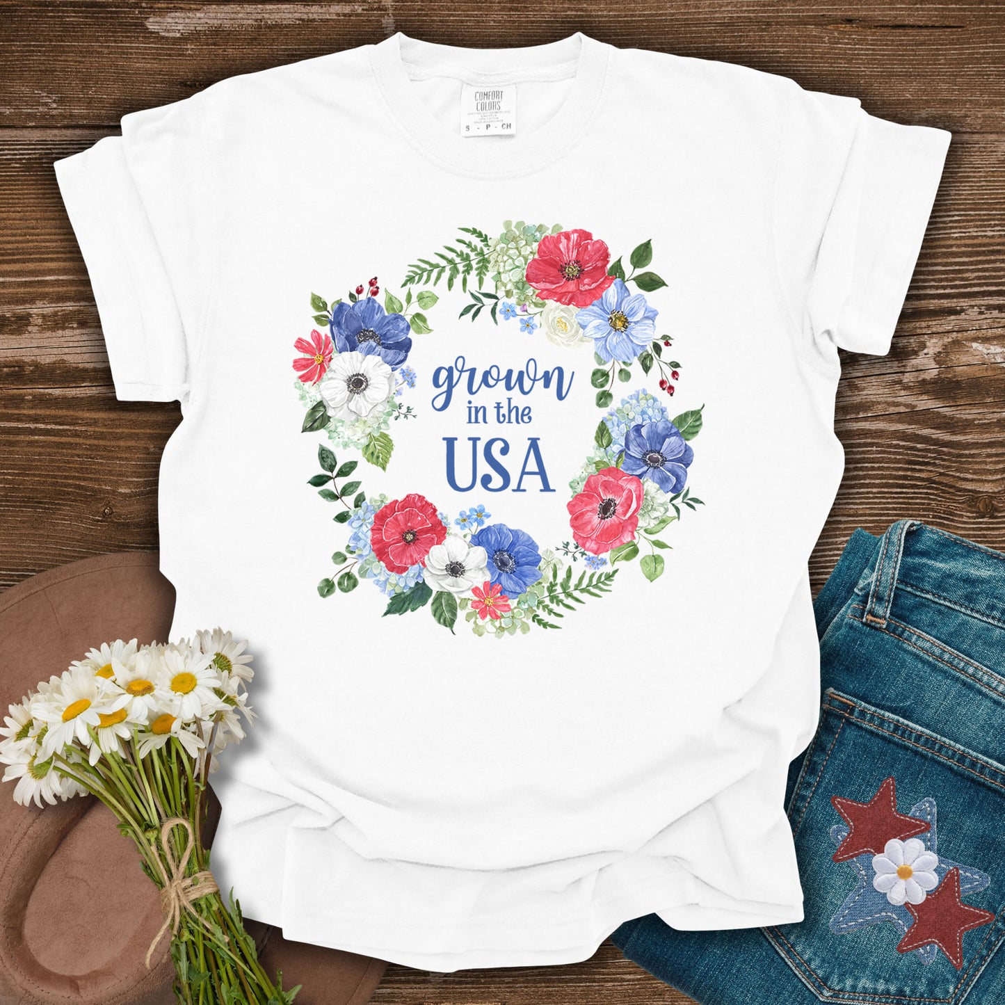 White S-sized cotton t-shirt with "Grown in the USA" in a floral wreath of red, white, and blue flowers.