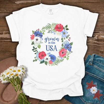 White S-sized cotton t-shirt with "Grown in the USA" in a floral wreath of red, white, and blue flowers.