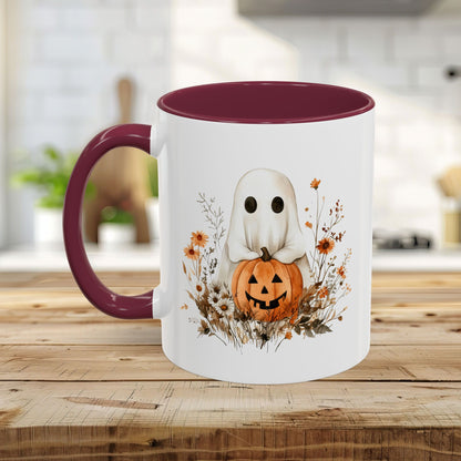 White ceramic mug with a watercolor ghost holding a jack-o'-lantern, surrounded by orange wildflowers. It has a contrasting burgundy handle and interior.