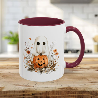 White ceramic 11oz mug with maroon handle and interior, featuring a watercolor ghost holding a jack-o'-lantern amidst autumn wildflowers.