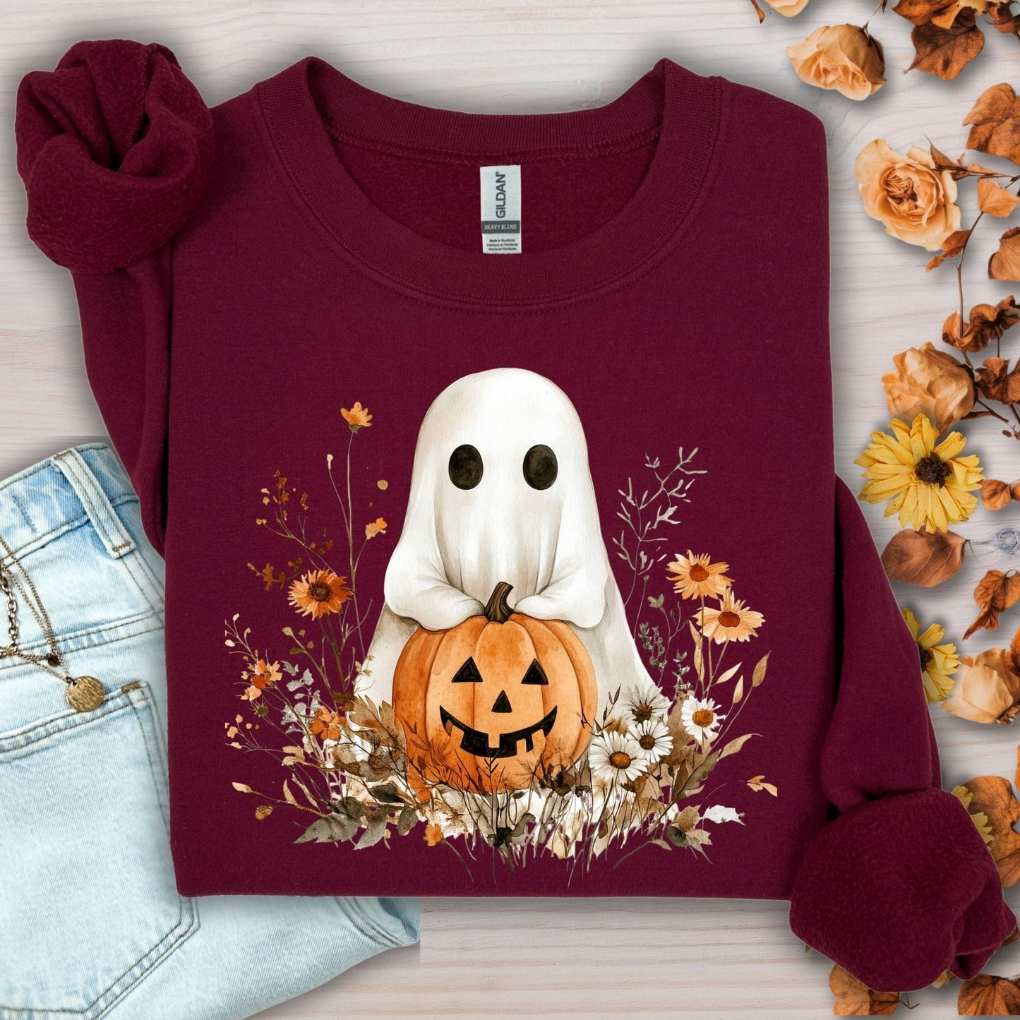 Maroon Gildan sweatshirt with a cute boho ghost holding a jack-o'-lantern, surrounded by autumn wildflowers.