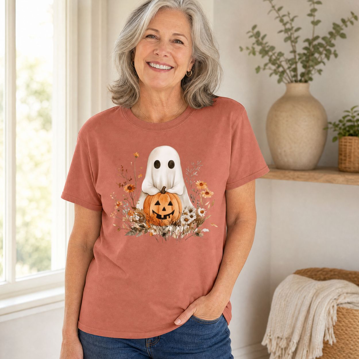 Woman in a relaxed-fit, rust-colored cotton t-shirt with a boho ghost holding a jack o'lantern and autumn florals.