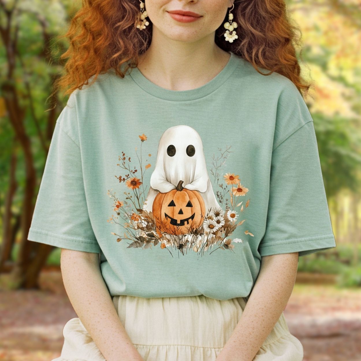 Boho ghost holding a jack o'lantern, surrounded by autumn florals, on a relaxed-fit sage green cotton t-shirt.