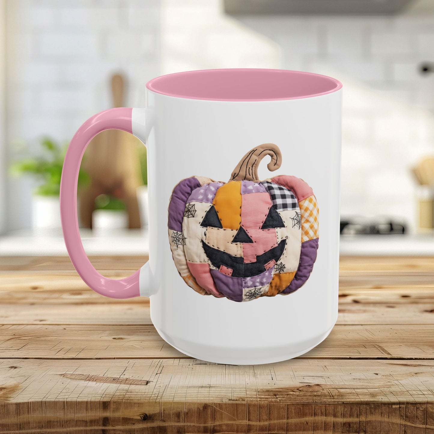 White ceramic mug with pink handle and interior, featuring a colorful quilted jack-o'-lantern design.