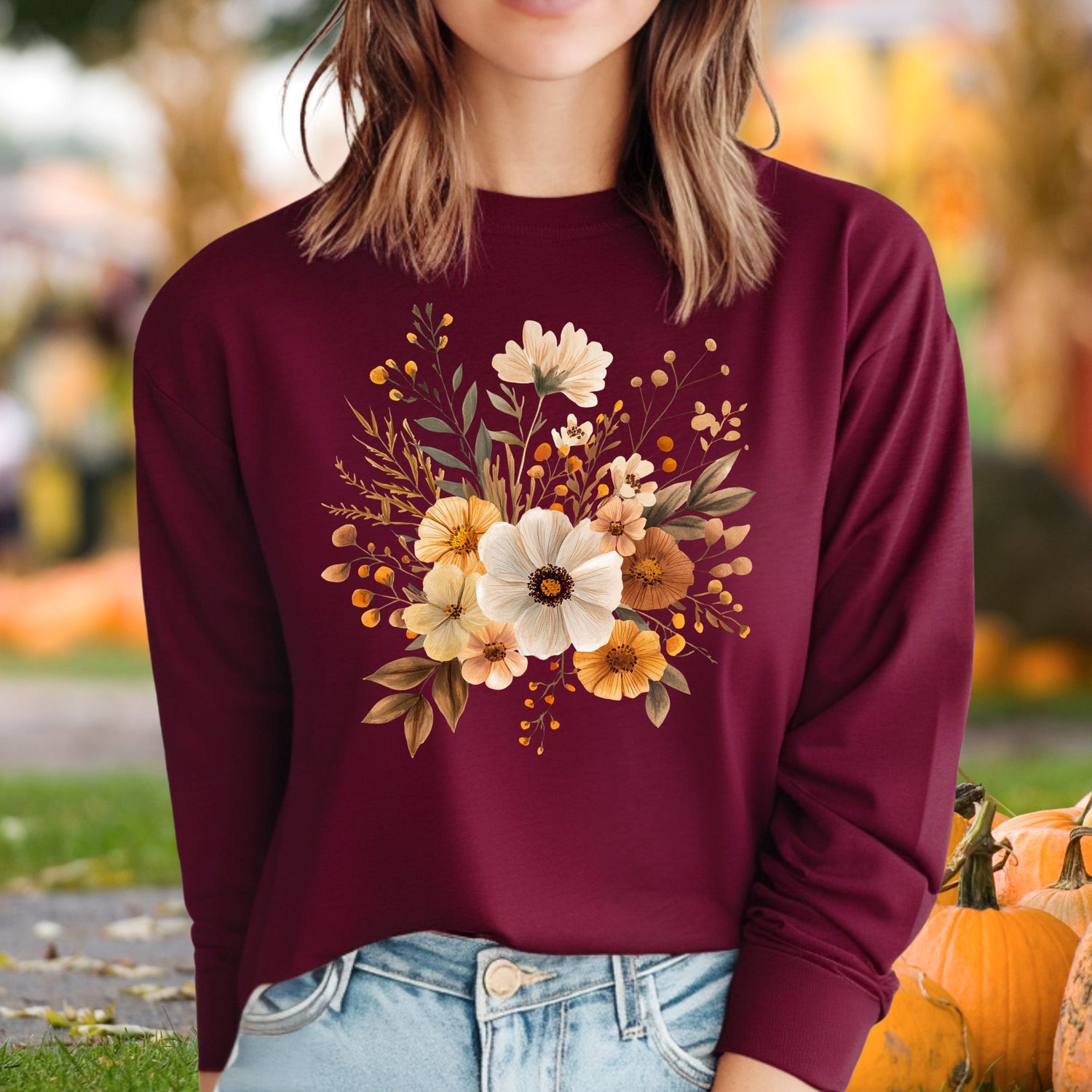 Woman wearing a maroon long-sleeve tee with a muted autumn floral design, paired with jeans.