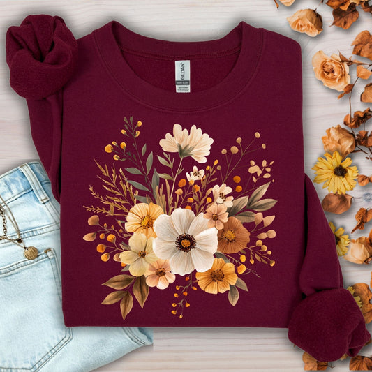Maroon Gildan sweatshirt with a watercolor autumnal floral design, next to jeans and fall foliage.