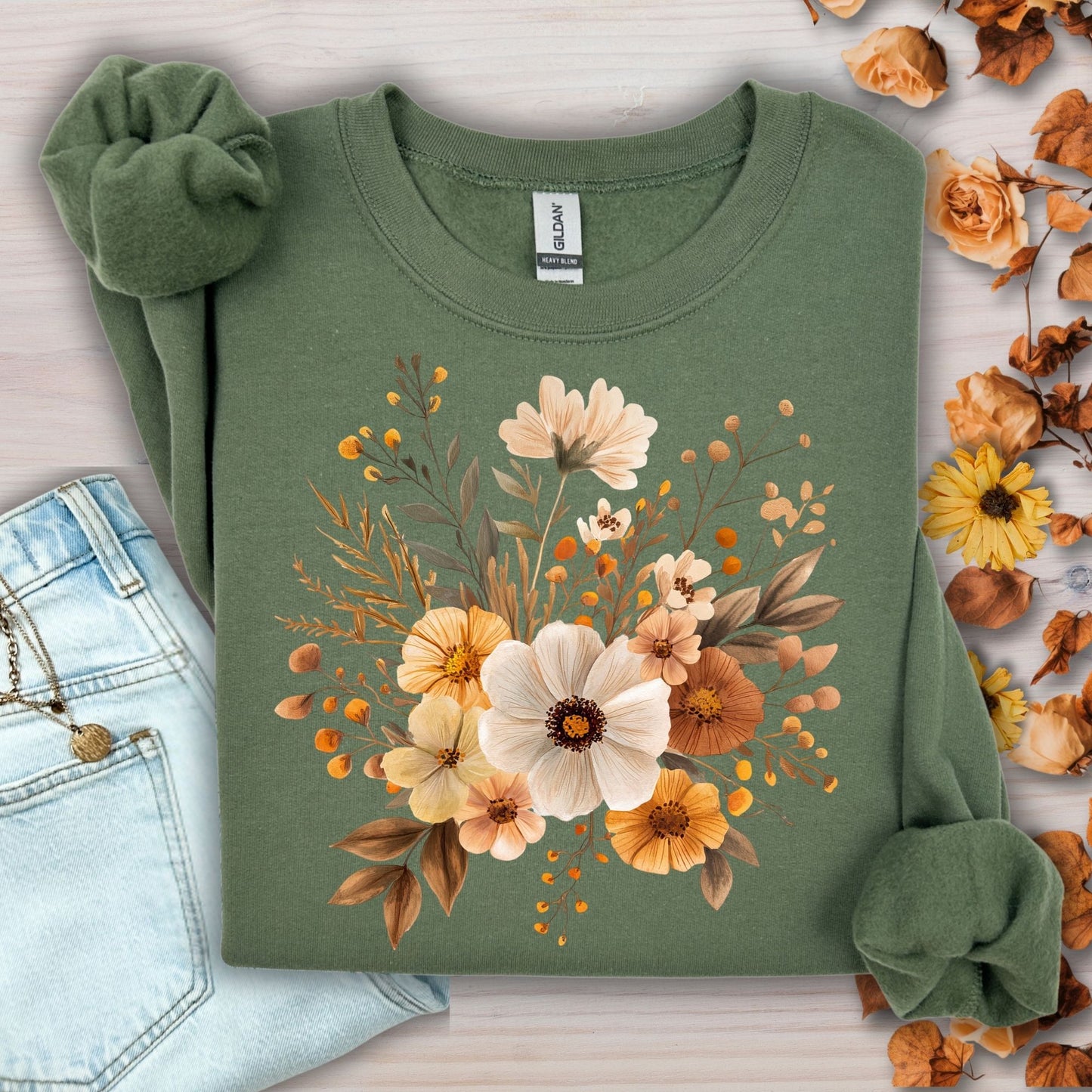 Military Green Harvest Blooms sweatshirt with watercolor autumnal flowers, next to jeans and fall leaves.