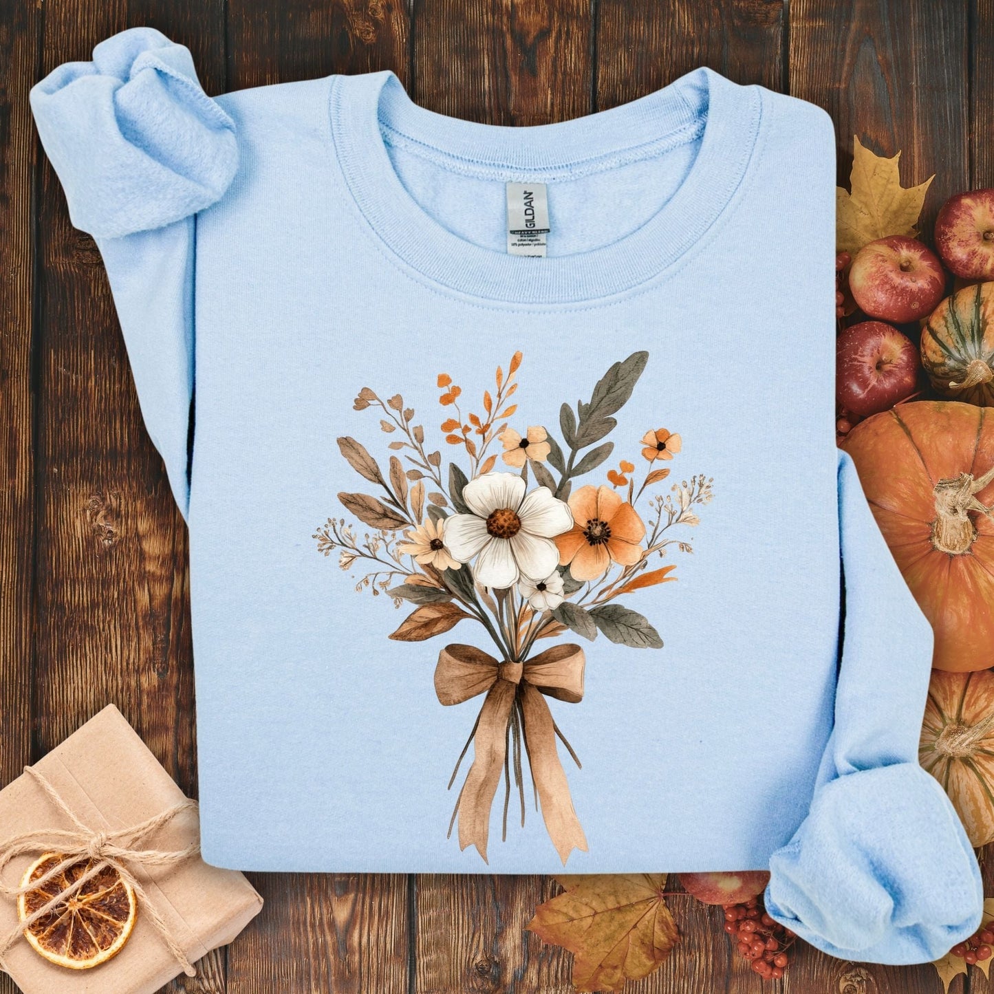 Light blue sweatshirt with a watercolor-inspired autumn floral bouquet tied with a brown bow.