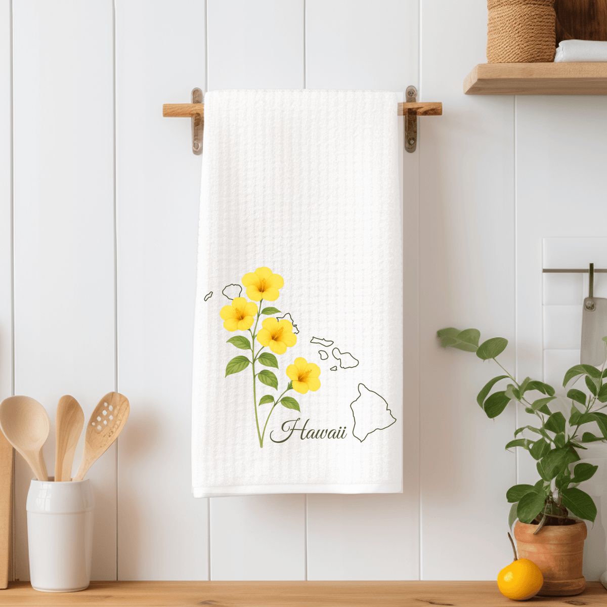 White microfiber tea towel with yellow hibiscus flowers and a subtle Hawaii map, hanging on a wooden rack.