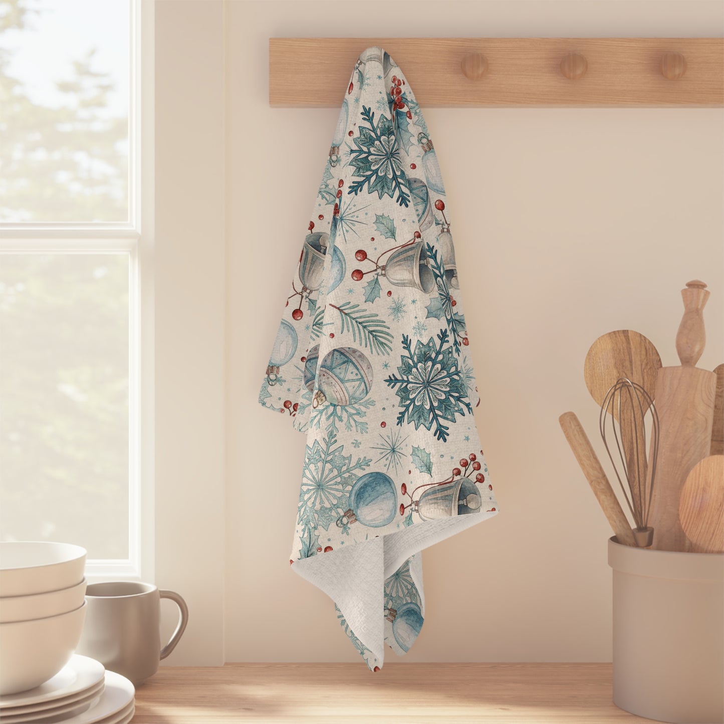 Microfiber tea towel with blue and silver holiday bells, snowflakes, and pine sprigs, hanging on a wooden peg.