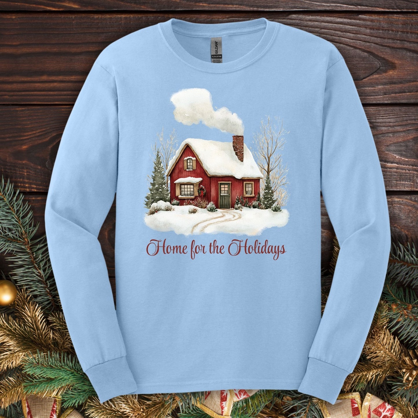 Light blue Gildan long sleeve tee with a watercolor red cabin, evergreens, and "Home for the Holidays" script.