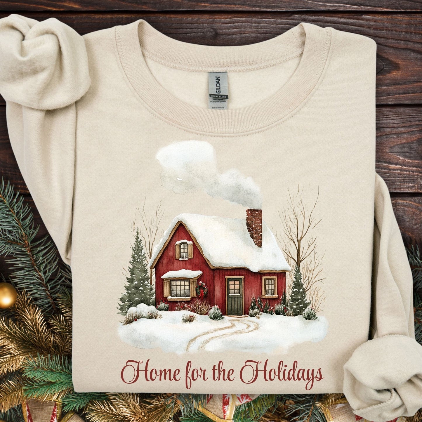 Sand Gildan fleece sweatshirt with vintage watercolor red cabin and "Home for the Holidays" text.