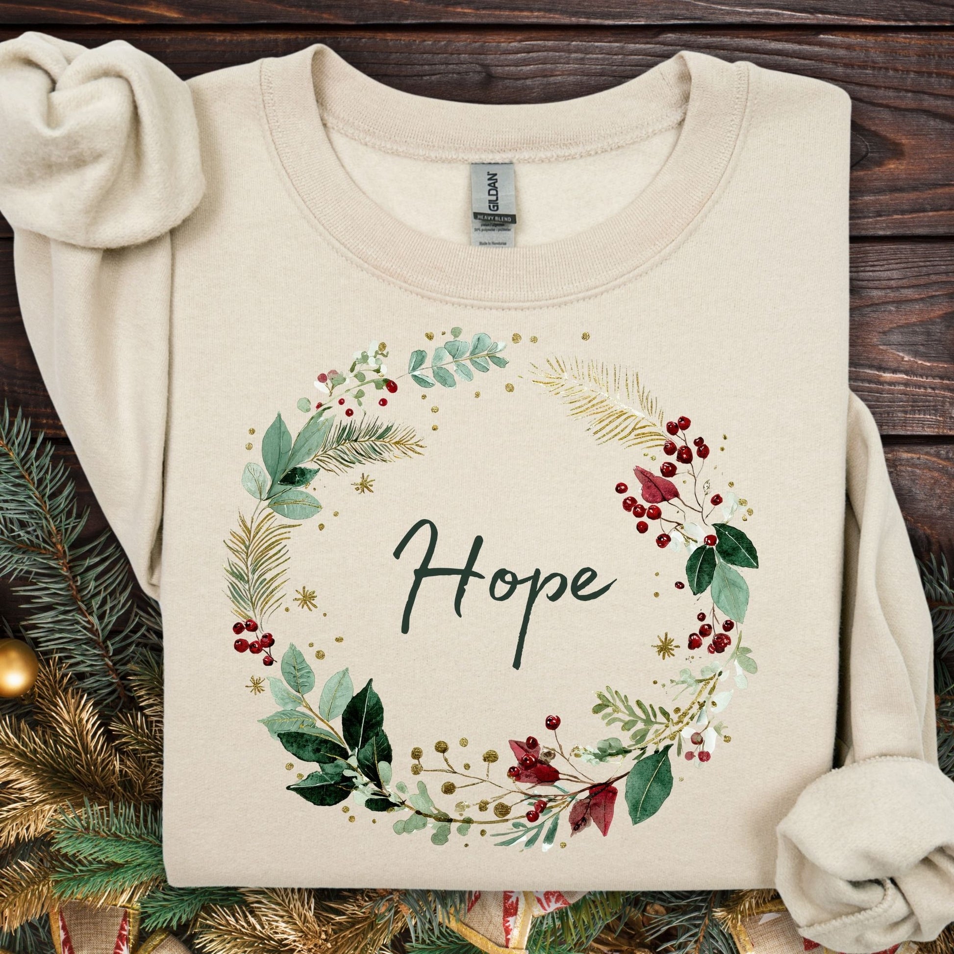 Sand Gildan sweatshirt with a watercolor Christmas wreath design encircling "Hope" in green, cream, gold, and red.