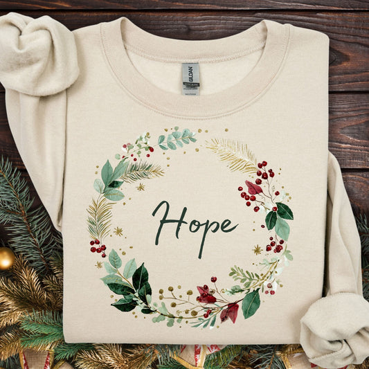 Sand Gildan sweatshirt with a watercolor Christmas wreath design encircling "Hope" in green, cream, gold, and red.