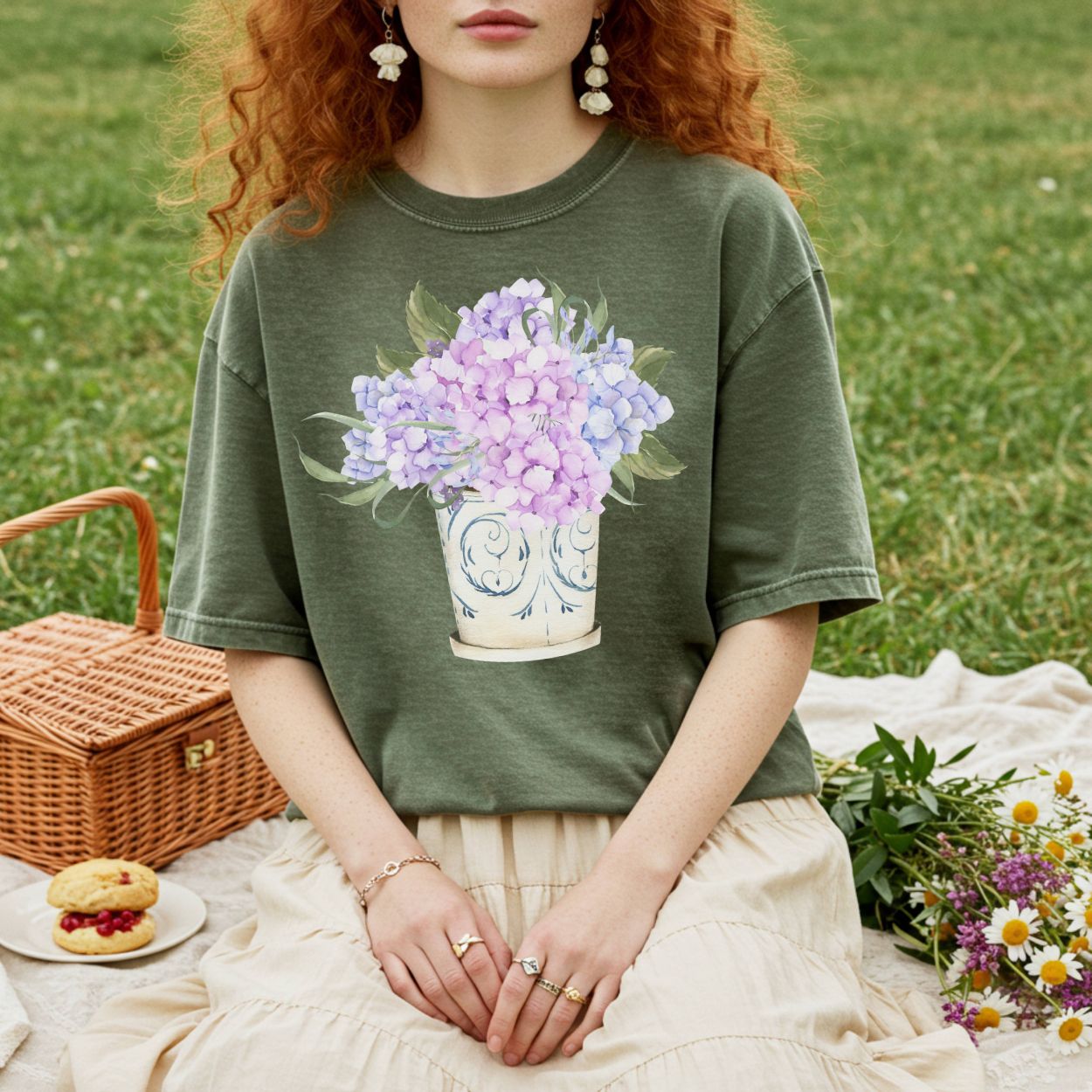 Garment-dyed olive green t-shirt with a watercolor-style lilac and blue hydrangea bouquet in a vintage vase.
