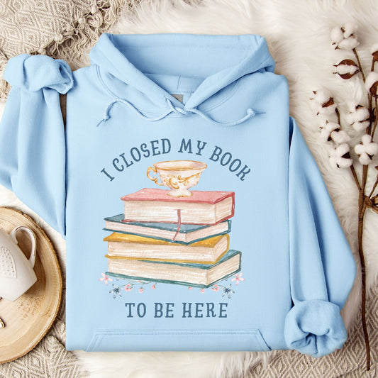 Light blue Gildan 18500 hoodie with "I Closed My Book To Be Here" text and stacked books graphic.