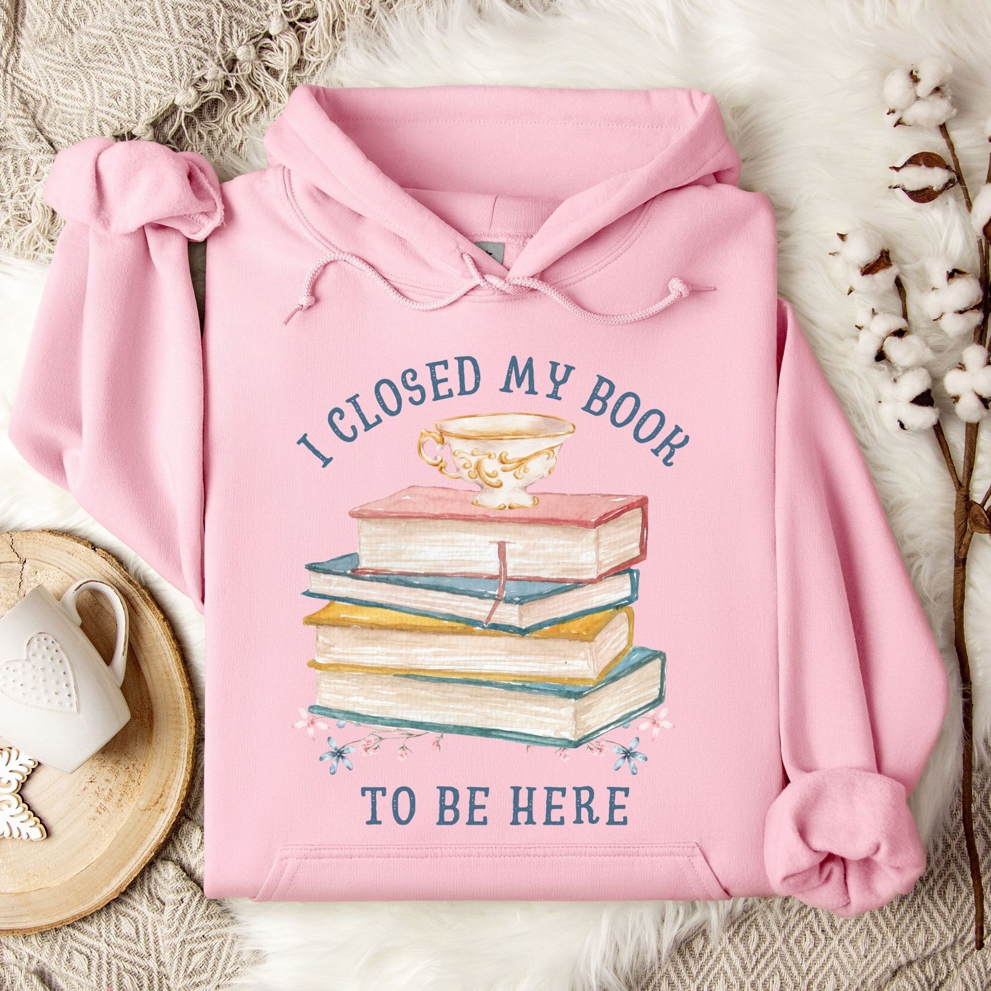 Light pink Gildan 18500 hoodie with "I Closed My Book To Be Here" text and book stack graphic.