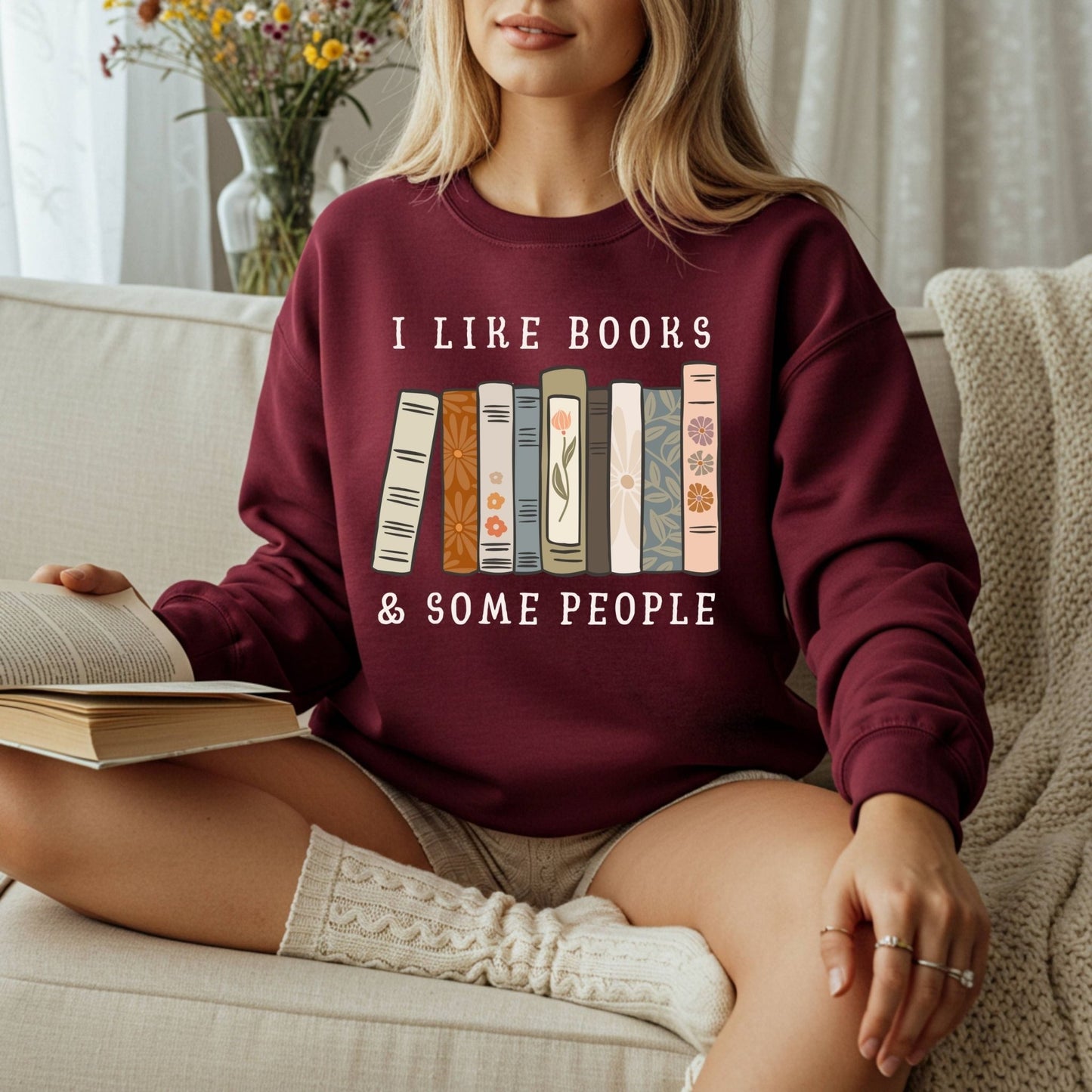 Maroon Gildan crewneck sweatshirt with "I like books & some people" and vintage book graphic, worn by a woman reading.