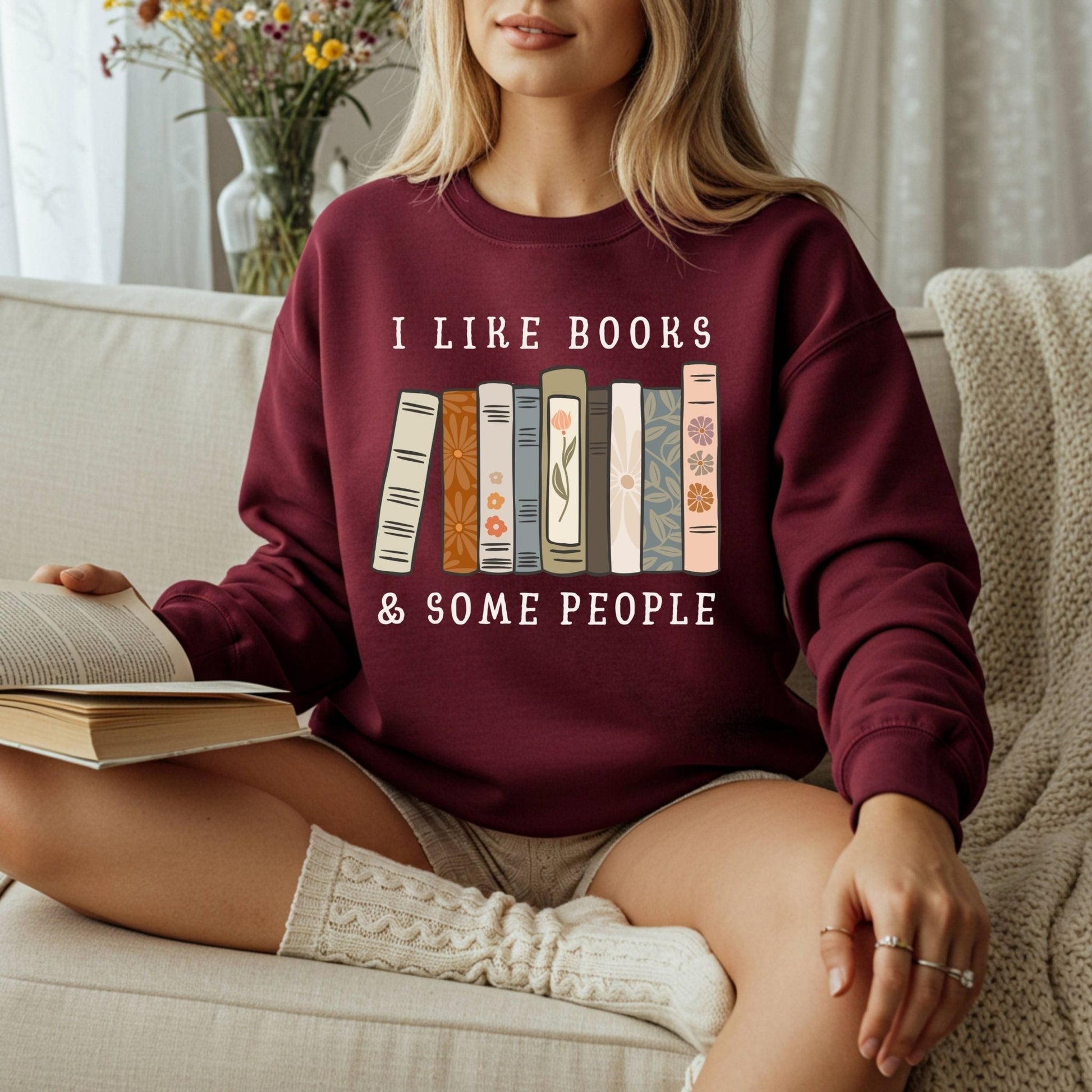 Maroon Gildan crewneck sweatshirt with "I like books & some people" and vintage book graphic, worn by a woman reading.