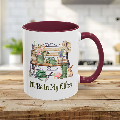 11oz ceramic gardener mug with maroon interior/handle, featuring "I'll Be In My Office" and garden tools illustration.