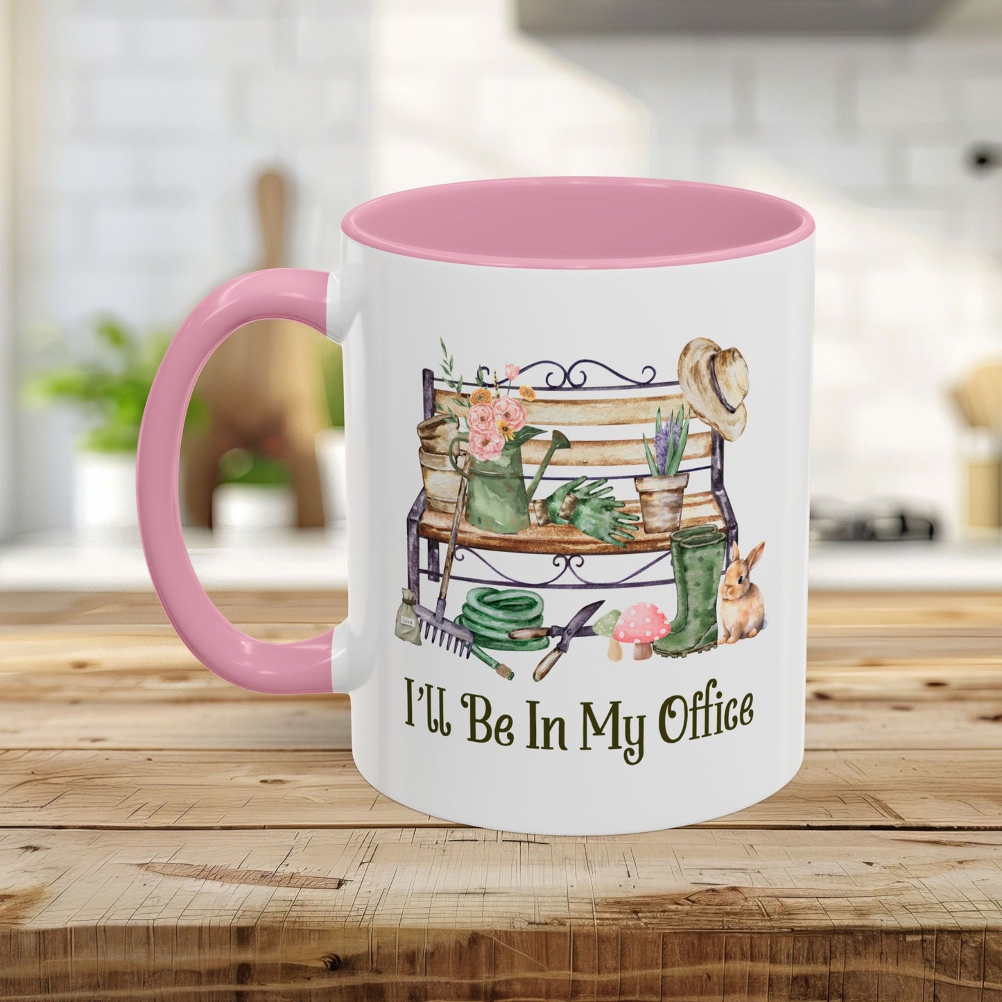 White ceramic 11oz mug with pink handle and interior, featuring watercolor gardening tools, bench, and "I'll Be In My Office" text.