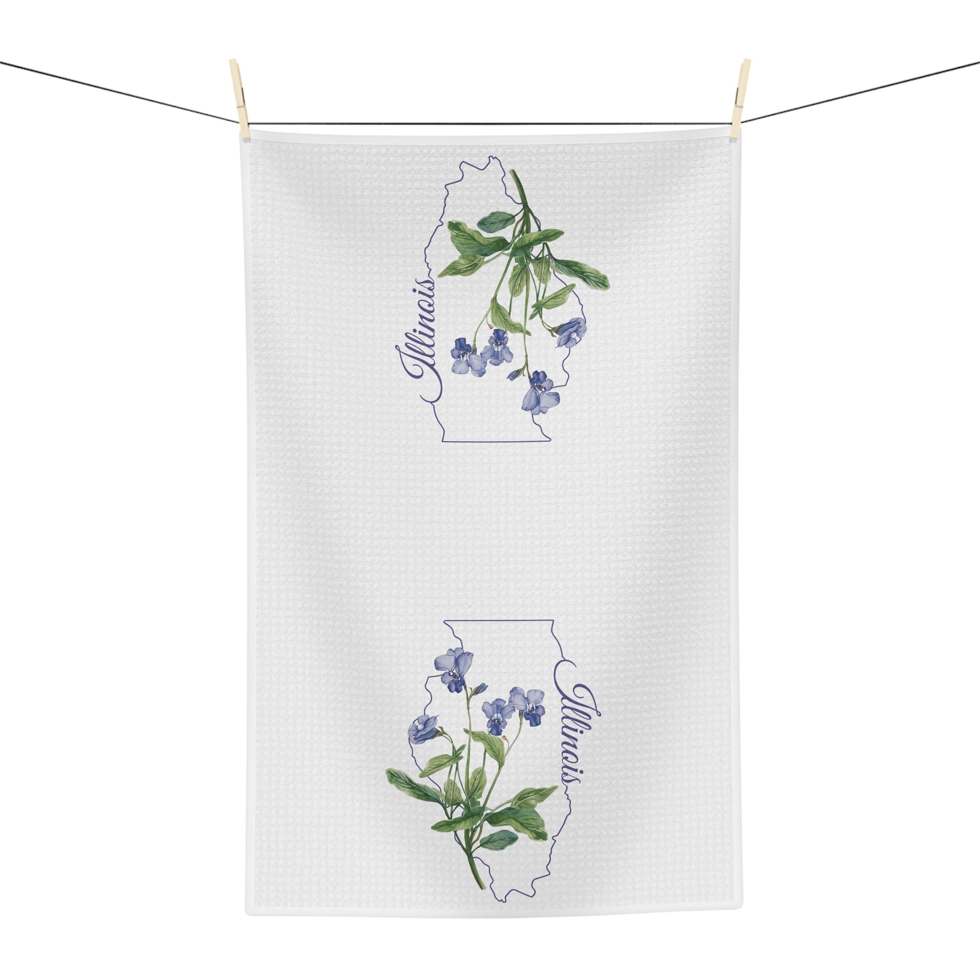 White microfiber tea towel with watercolor blue violets over an Illinois state outline, hanging on a clothesline.