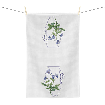 White microfiber tea towel with watercolor blue violets over an Illinois state outline, hanging on a clothesline.