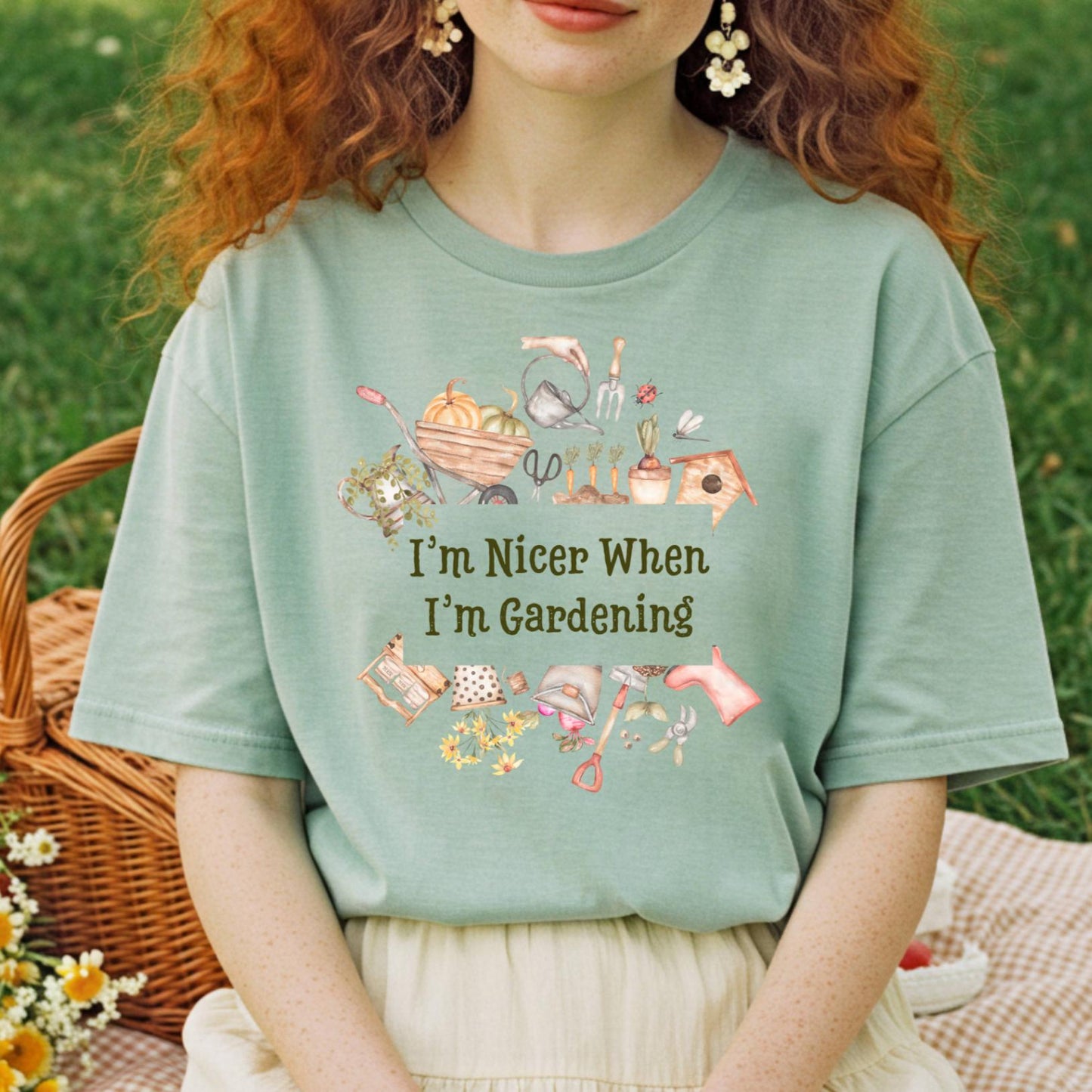 woman with red, curly hair wearing a light green t-shirt with gardening-themed text and graphics, sitting outdoors at a picnic