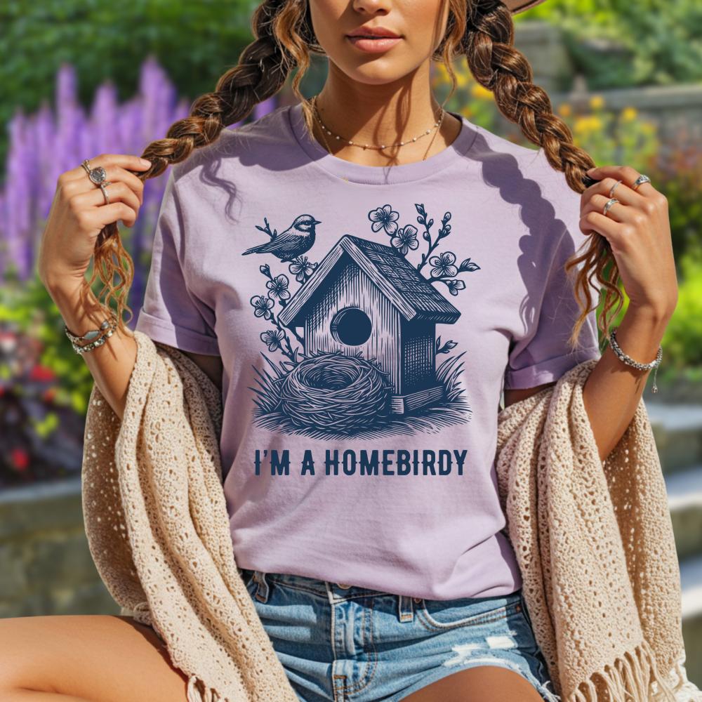 Woman wearing a purple t-shirt with a birdhouse design and text, standing outdoors.