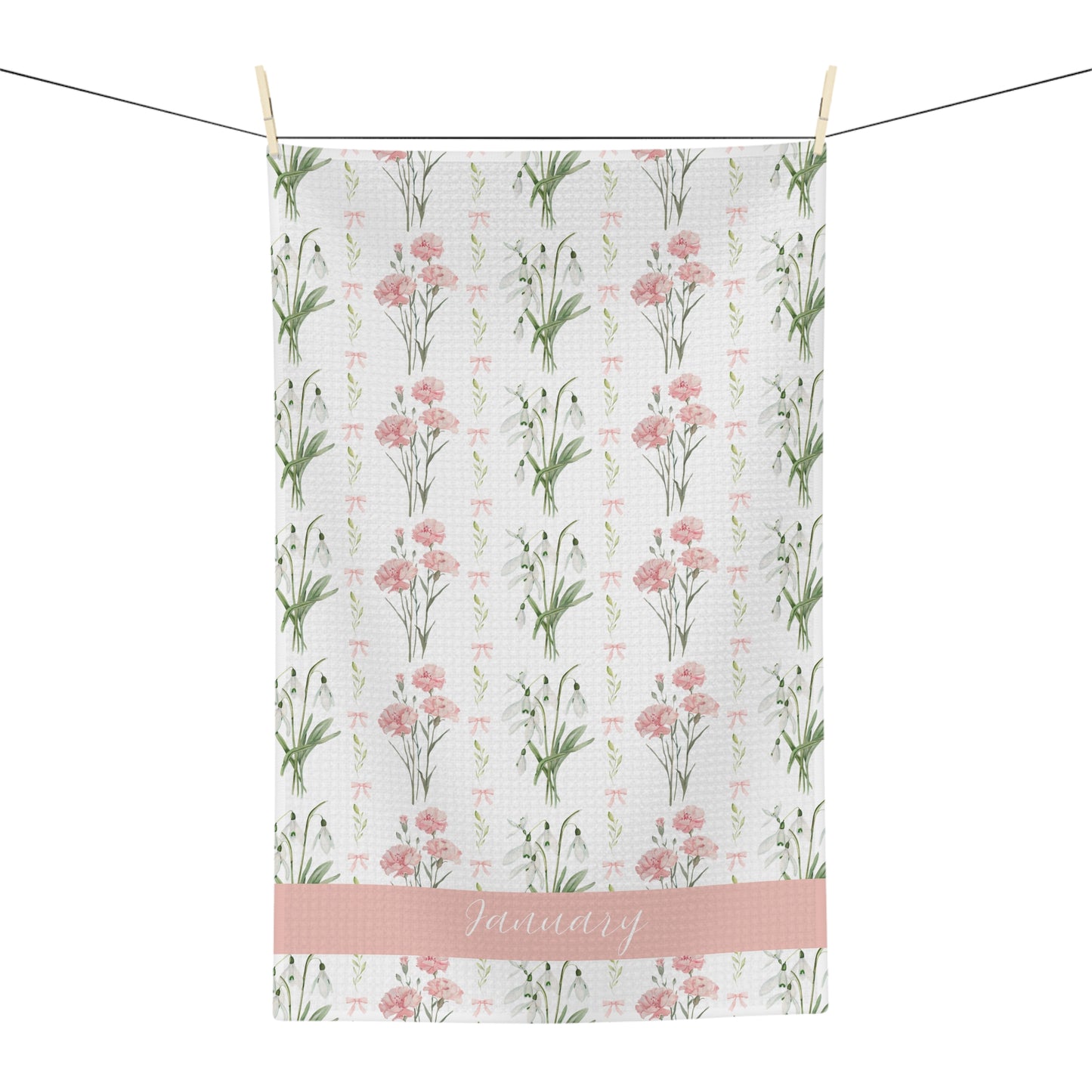White microfiber tea towel with pink carnations, snowdrops, and "January" script, hanging on a line.