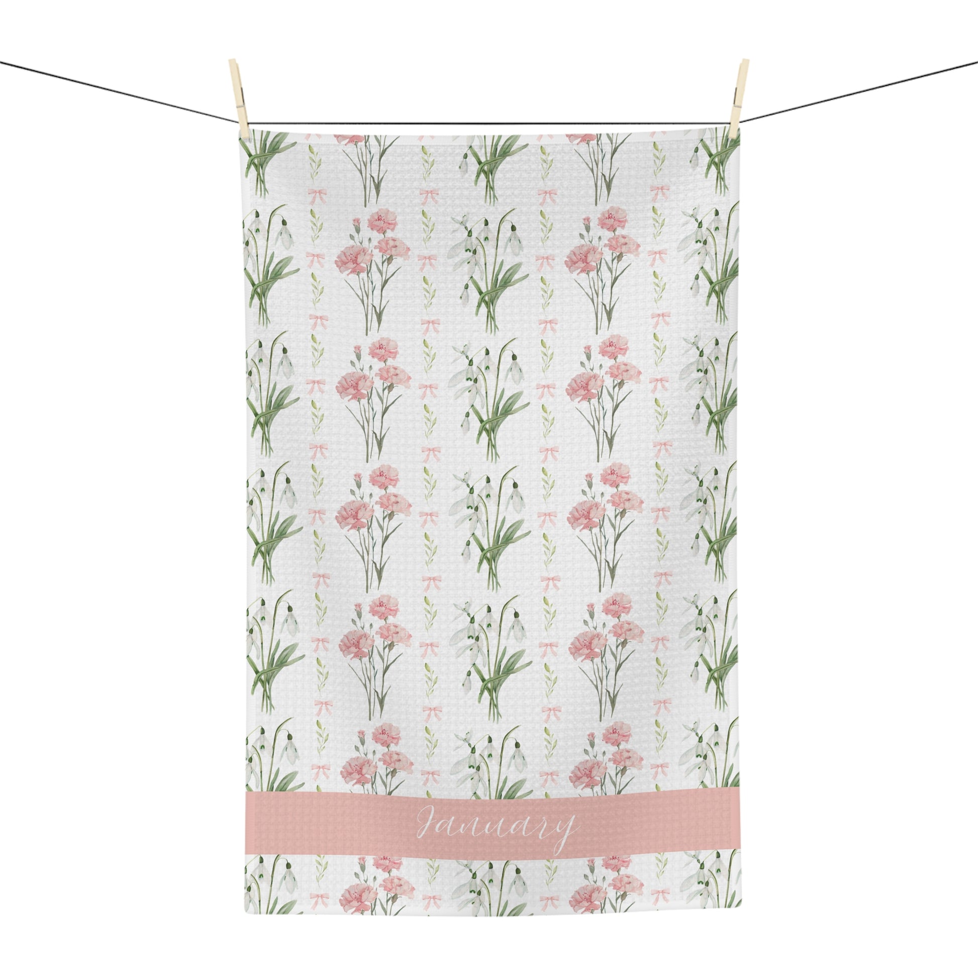 White microfiber tea towel with pink carnations, snowdrops, and "January" script, hanging on a line.
