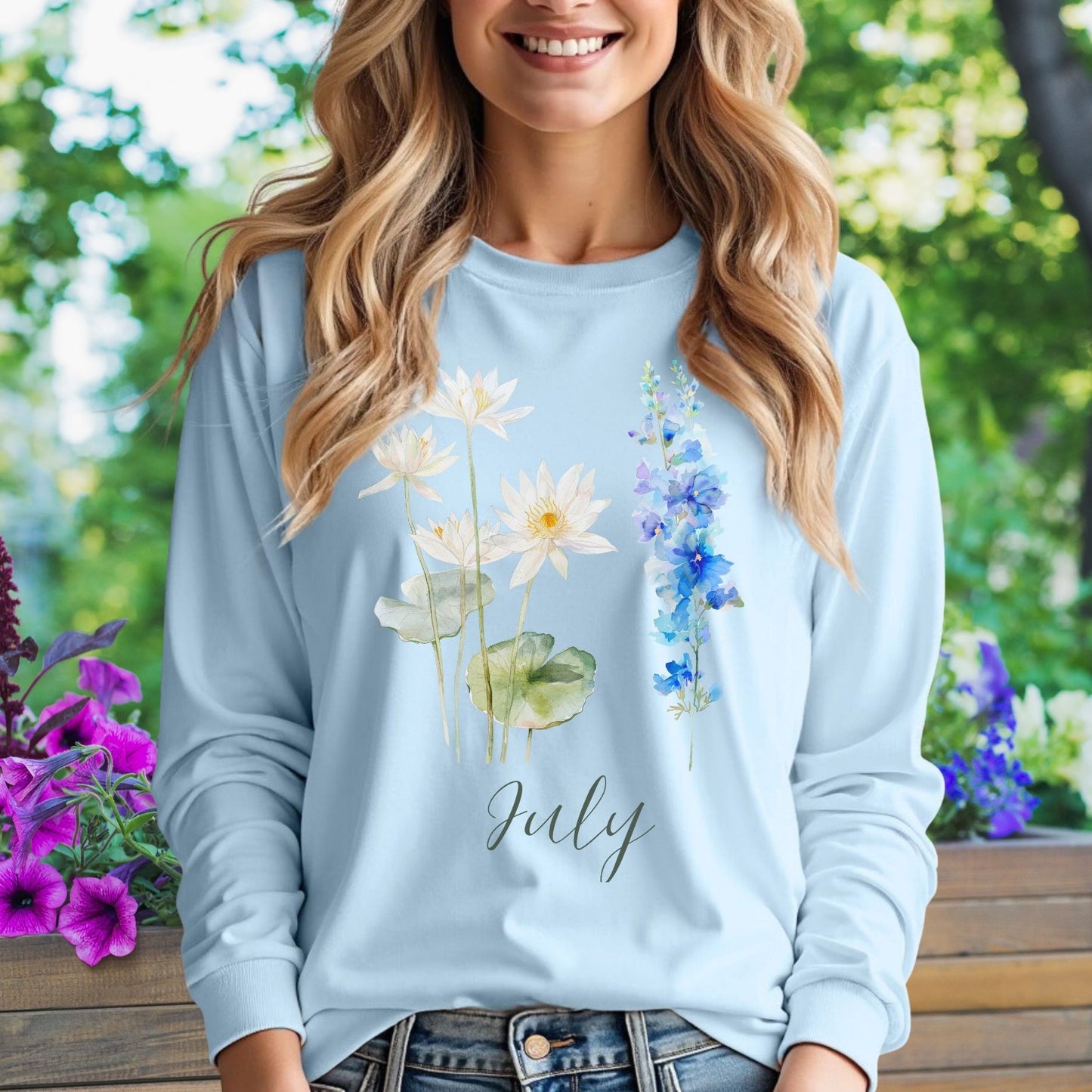 Woman in light blue long-sleeve tee with watercolor waterlily and larkspur flowers and "July" text.