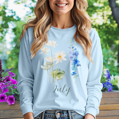 Woman in light blue long-sleeve tee with watercolor waterlily and larkspur flowers and "July" text.