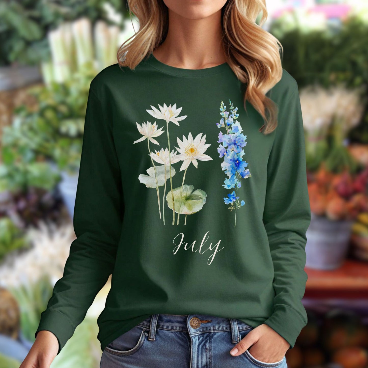 Woman in a dark green long-sleeve tee with watercolor waterlily, larkspur, and "July" text.