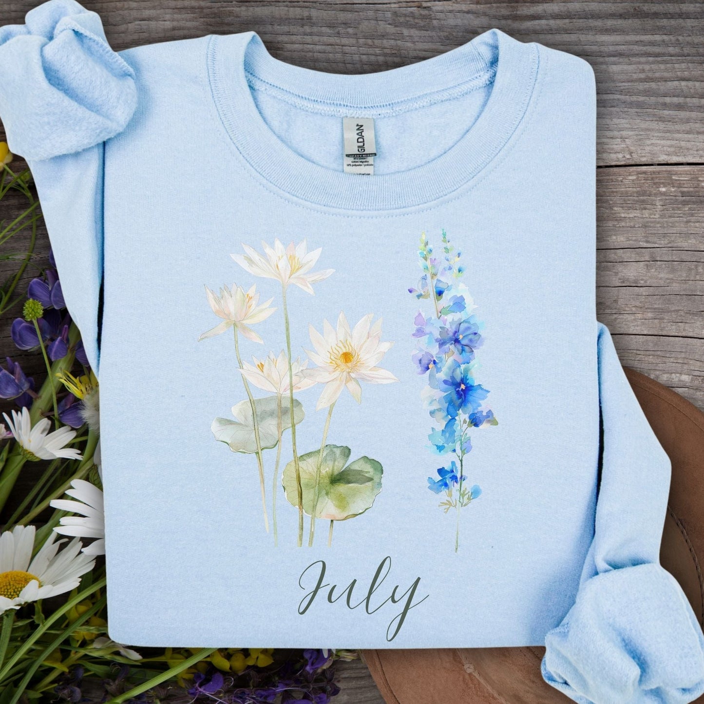 Light blue cotton-poly sweatshirt with watercolor waterlilies, larkspur, and "July" text.