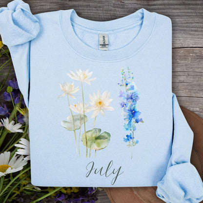 Light blue cotton-poly sweatshirt with watercolor waterlilies, larkspur, and "July" text.