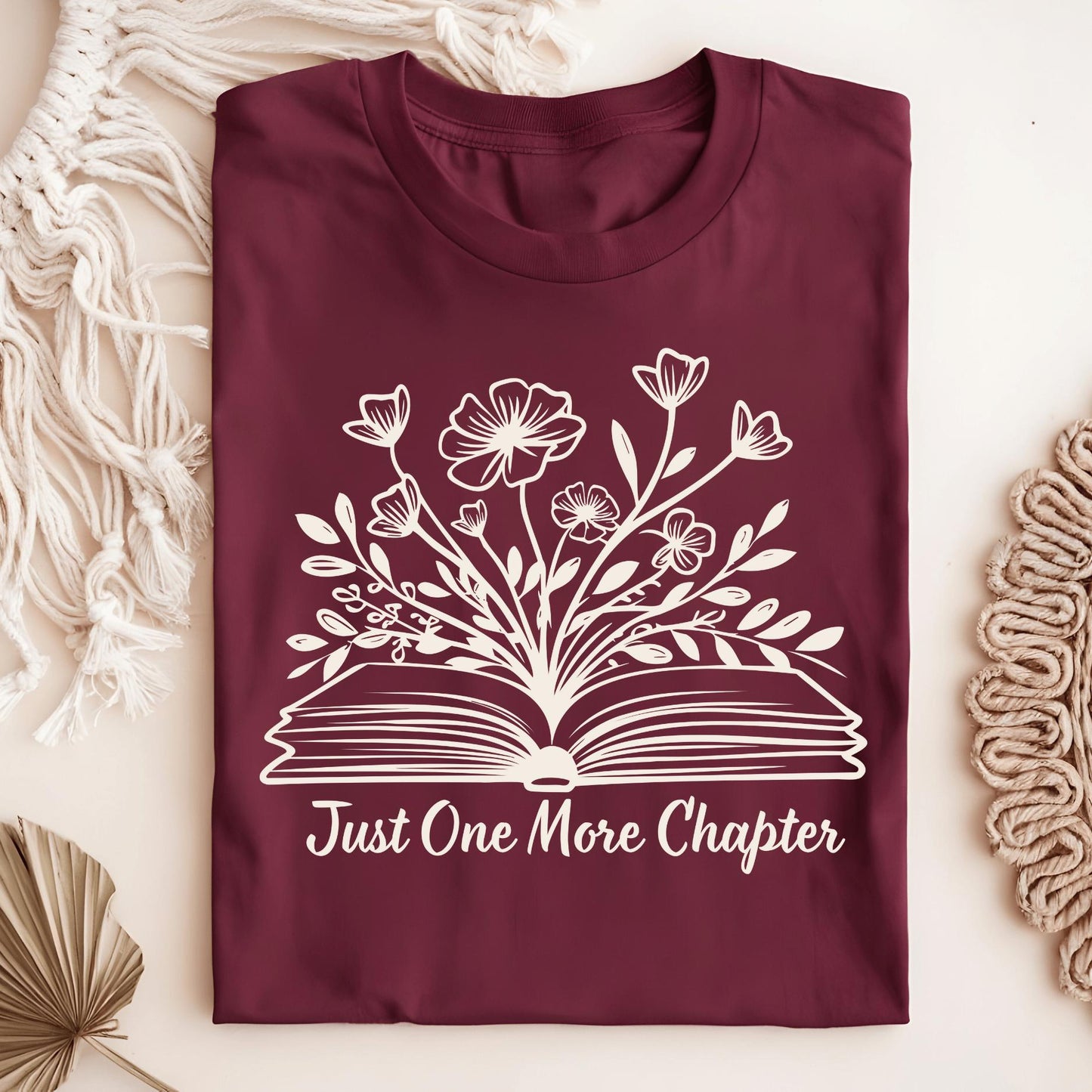 Maroon Just One More Chapter T-shirt with white outline of a book and wildflowers.