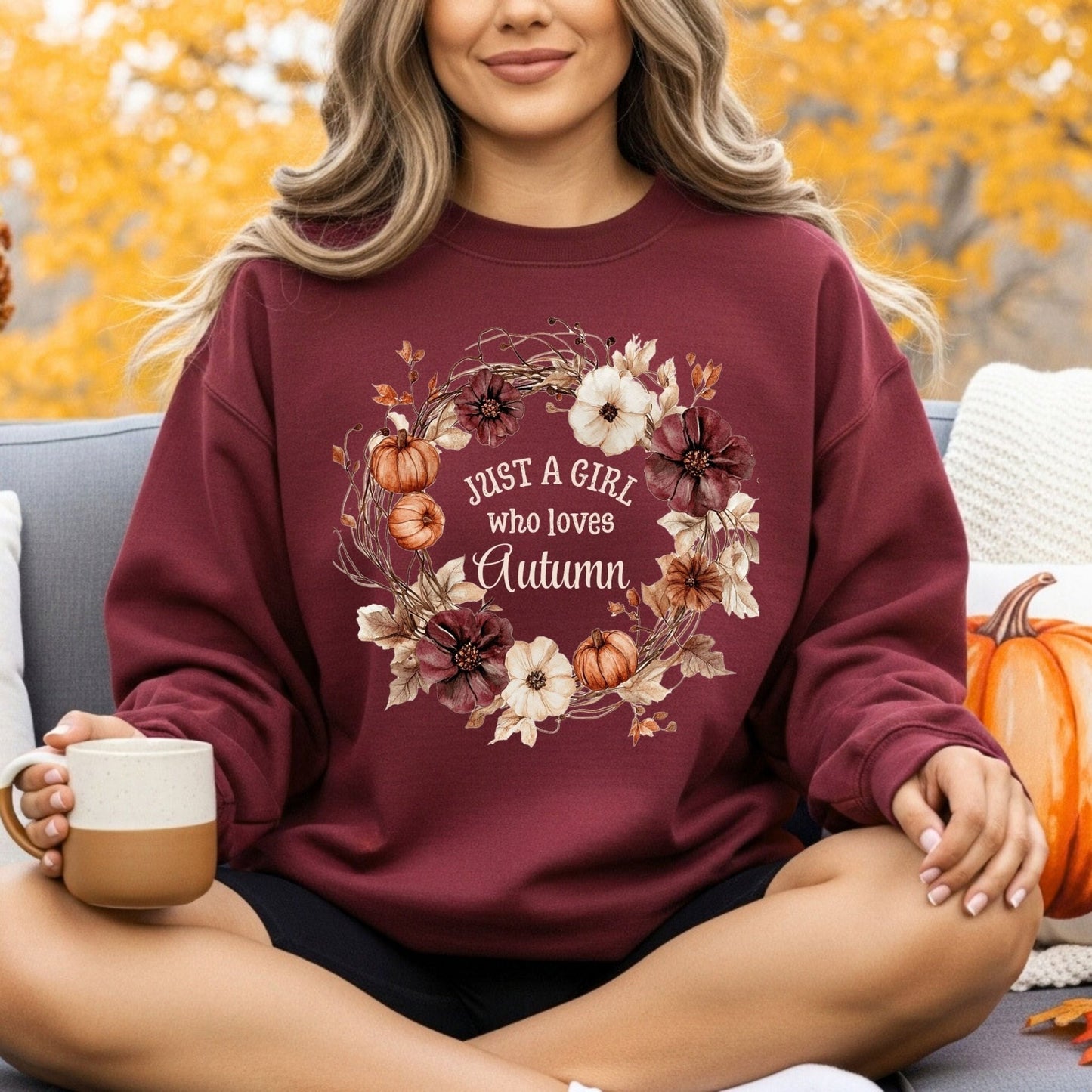 Woman in a maroon "Just a Girl Who Loves Autumn" sweatshirt with a watercolor floral wreath and pumpkins.